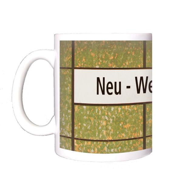 U-Bahnhof Neu-Westend Kaffeetasse - schwarze Schrift auf weißem Schild, vor grün-orange-weiß getupfter Wand