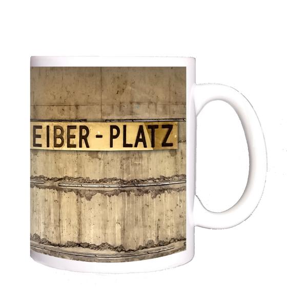 U-Bahnhof Walther-Schreiber-Platz Kaffeetasse - ehemalige Stationsgestaltung, schwarze Schrift auf Messingschild vor grau-brauner Betonwand