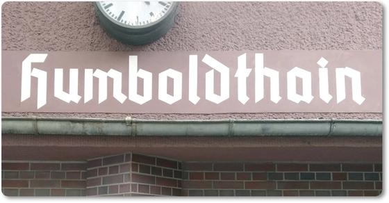 S-Bahnhof Humboldthain - weiße Schrift auf altrosa-farbende Fassade darüber eine Uhr darunter Backstein Wand