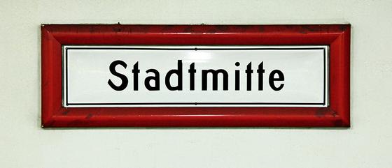U-Bahnhof Stadtmitte Kaffeetasse - schwarze Schrift auf weißem Schild, mit rotem dickem Rahmen, vor weißer Wand