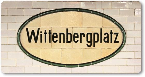 U-Bahnhof Wittenbergplatz Kühlschrankmagnet - schwarze Schrift auf beigem, ovalem Schild mit dunklem Rand, als Teil einer weißen Fliesenwand
