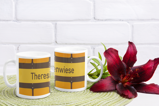 U-Bahnhof Theresienwiese Tasse - schwarze Schrift auf gelbem Schild, vor gelbem Hintergrund mit schwarzen Umrandungen