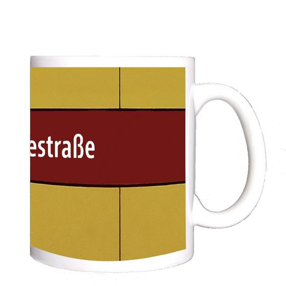 U-Bahnhof Quiddestraße Kaffeetasse - weiße Schrift auf dunkelrotem Streifen, vor gelber Plattenwand