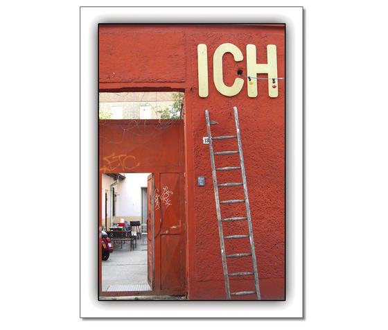 Klassische Postkarte -Die Lebensaufgabe: Finden des eigenen Ichs. Abgebildet sind eine rote Wand an welcher eine Holzleiter zum Schriftzug "Ich" steht. 