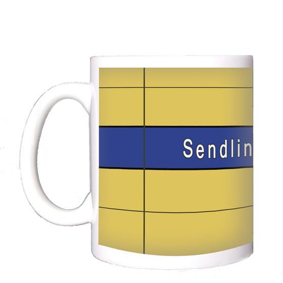 U-Bahnhof Sendlinger Tor Kaffeetasse - weiße Schrift auf blauem Streifen, vor gelber Plattenwand
