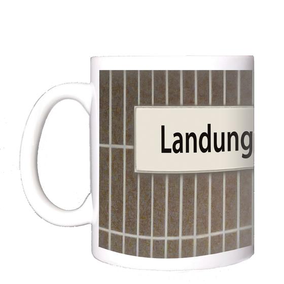 U-Bahnhof Landungsbrücken Kaffeetasse - schwarze Schrift auf weißem Schild vor braun-grauer Fliesenwand