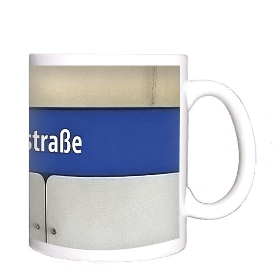 U-Bahnhof Poccistraße Kaffeetasse - weiße Schrift auf dunkelblauem Streifen, vor weißer Plattenwand