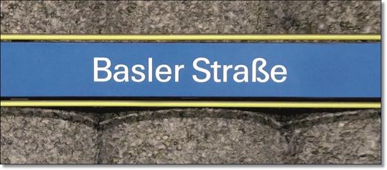 U-Bahnhof Basler Straße Kaffeetasse - weiße Schrift auf hellblauem Schild, gelb umrandet, vor grauer Säulenwand