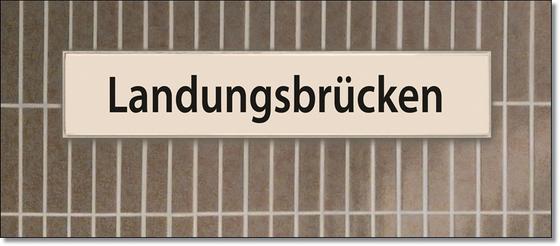 U-Bahnhof Landungsbrücken Kaffeetasse - schwarze Schrift auf weißem Schild vor braun-grauer Fliesenwand