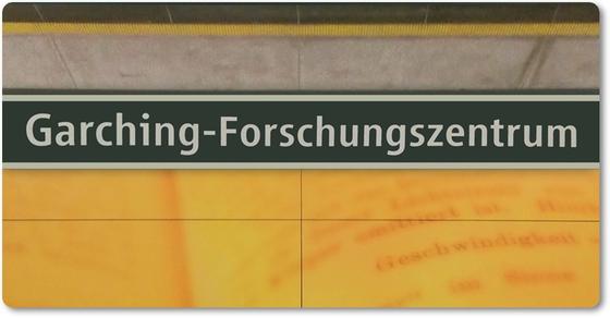 U-Bahnhof Garching-Forschungszentrum Kaffeetasse - weiße Schrift auf schwarzem Schild, zwischen gelblicher Plattenwand mit Buchseiten-Print und grauen Platten