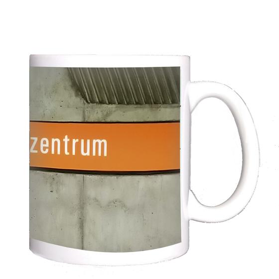 U-Bahnhof Olympiazentrum München Kaffeetasse - weiße Schrift auf orangem Schild vor grauer Betonwand