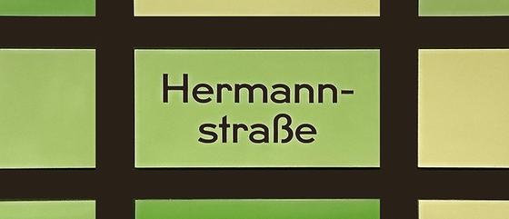 U-Bahnhof Hermannstraße Kaffeetasse - schwarze Schrift vor grün-gelbem Hintergrund mit schwarzem Gittermuster