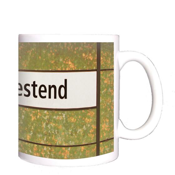 U-Bahnhof Neu-Westend Kaffeetasse - schwarze Schrift auf weißem Schild, vor grün-orange-weiß getupfter Wand