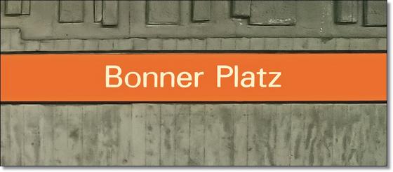 U-Bahnhof Bonner Platz Kaffeetasse - weiße Schrift auf orangem Streifen, vor grauer Betonwand