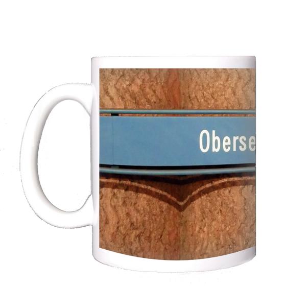U-Bahnhof Obersendling Kaffeetasse - weiße Schrift auf blauem Schild, vor Betonsäulen-Wand