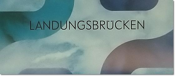 S-Bahnhof Landungsbrücken Kaffeetasse - schwarze Schrift auf blassblauem Hintergrund mit roten und blauen Schlangenlinien