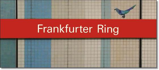 U-Bahnhof Frankfurter Ring München - weiße Schrift auf rotem Balken mit blauem Vogel darauf,vor Mosaikwand mit blauen, beigen und weißen Streifen
