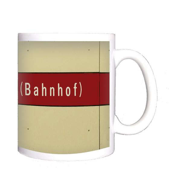 U-Bahn-Tasse Giesing Bahnhof - weiße Schrift auf dunkelrotem Streifen vor beigem Hintergrund