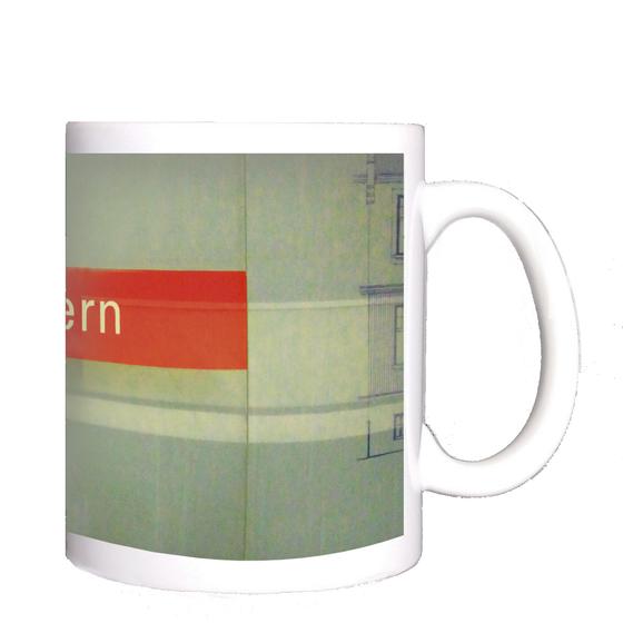 U-Bahnhof Gern Kaffeetasse - weiße Schrift auf rotem Schild, vor grauer Steinwand, mit blauer Zeichnung auf der linken Seite