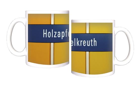 U-Bahn-Tasse mit dem Schriftzug des Muenchner Bahnhofs Holzapfelkreuth der Linie U6 - Dunkelblaues Schild mit weissem Text auf orangenem Grund  