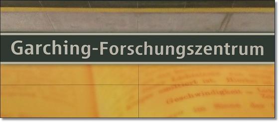 U-Bahnhof Garching-Forschungszentrum Kaffeetasse - weiße Schrift auf schwarzem Schild, zwischen gelblicher Plattenwand mit Buchseiten-Print und grauen Platten