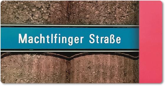 U-Bahnhof Machtlfinger Strasse Kühlschrankmagnet - weiße Schrift auf blauem Schild, vor Betonsäulen-Wand mit pinkem Streifen