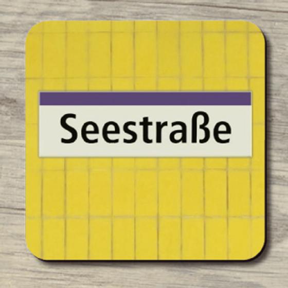 U-Bahnhof Seestraße - schwarze Schrift auf weißem Schild oben ein lila Streifen im Hintergrund gelbe Fliesen