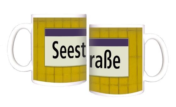 U-Bahnhof Seestraße Kaffeetasse - schwarze Schrift auf weißem Schild mit lila Streifen, vor gelber Mosaikwand