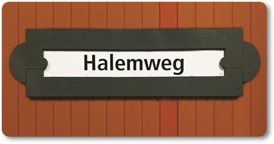 U-Bahn-Magnet Berlin Halemweg - schwarze Schrift auf traditionellem Schild mit Einkerbung rechts und links, sowie schwarzer Umrandung, vor rot-braunem Lattenhintergrund