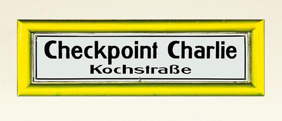 U-Bahnhof Checkpoint Charlie Kochstrasse Kaffeetasse - schwarze Schrift auf weißem Schild mit gelbem Rahmen, vor weisser Wand
