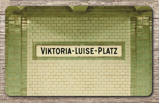U-Bahnhof Viktoria-Luise-Platz Frühstücksbrettchen - weißes, traditionelles Blechtschild mit schwarzer Schrift, vor weißer Fliesenwand, umrandet von grünen Kacheln