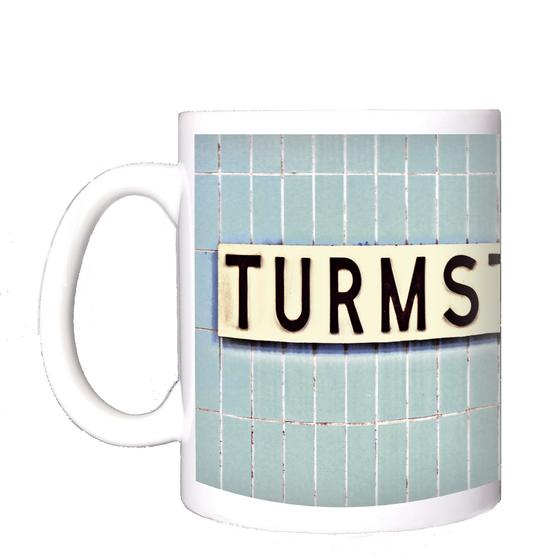 U-Bahnhof Turmstrasse Kaffeetasse - weißes Schild mit schwarzer, schlichter Schrift auf blauen Fliesen