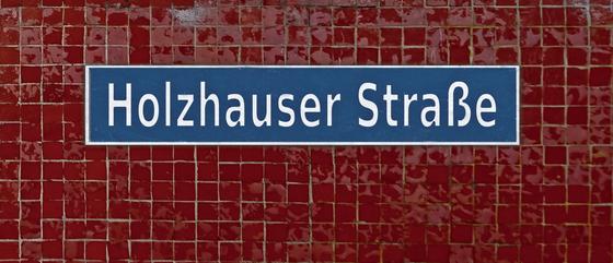 U-Bahnhof Holzhauser Straße - Weiße Schrift auf blauem Schild mit weißer Umrandung auf dunkelroten Fliesen - Ansicht links und rechts
