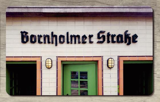 S-Bahnhof Bornholmer Strasse Aussenansicht S1 - Schwarze Buchstaben in Frakturschrift auf hellem Fliesengrund über drei knallig lachsfarbenen Türrahmen, zentrale grüne Tür ist geschlossen und bildet ein farbliches Highlight