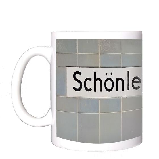 U-Bahnhof Schönleinstraße Kaffeetasse - schwarze Schrift auf weißem Schild vor fliederfarbenen quadratischen Kacheln