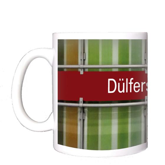 U-Bahnhof Dülferstraße Kaffeetasse - weiße Schrift auf rotem Schild auf Metallgestell, vor Streifenhintergrund in diversen Grüntönen