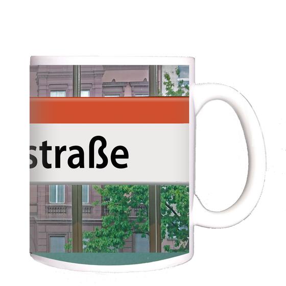 U-Bahnhof Kaffeetasse Bülowstrasse - schwarze Schrift auf weißem Schild mit orangem Streifen, an Bahnhofsfenster befestigt mit rotem und gelbem Haus im Hintergrund
