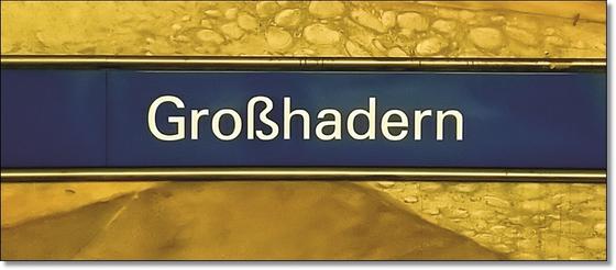 U-Bahnhof Großhadern Kaffeetasse - weiße Schrift auf dunkelblauem Streifen, vor gelber Wand mit Steinmuster