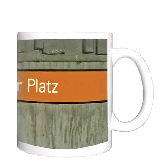 U-Bahnhof Bonner Platz Kaffeetasse - weiße Schrift auf orangem Streifen, vor grauer Betonwand
