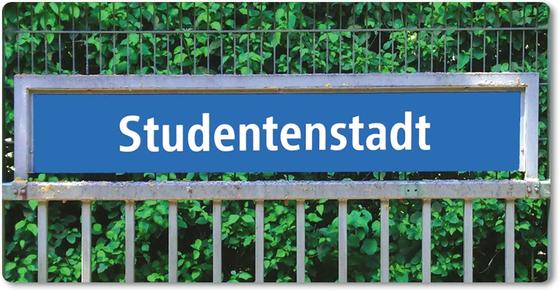 U-Bahnhof Studentenstadt - weiße Schrift auf blauem Schild an grauem Gitter, vor Bäumen