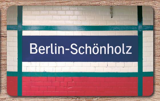 S-Bahnhof Schönholz Frühstücksbrettchen  Berlin - blaues Schild mit weißer Schrift auf weißem Backsteinhintergrund, umrandet von petrolfarbenen Streifen, roter Streifen am unteren Bildrand