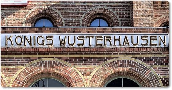S-Bahnhof Koenigswusterhause Kühlschrankmagnet braune Schrift auf grauem Streifen an Backsteinhaus mit Fenstern
