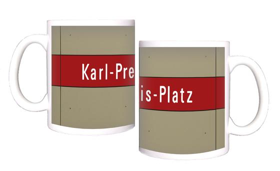 U-Bahnhof Karl-Preis-Platz Kaffeetasse - weiße Schrift auf dunkelrotem Streifen, vor grau-brauner Plattenwand