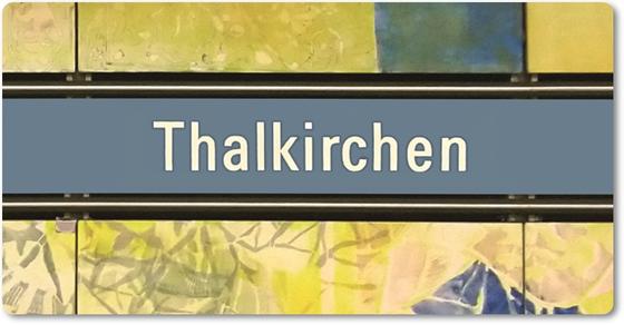 U-Bahnhof Thalkirchen Kühlschrankmagnet - weiße Schrift auf blauem Schild, mit schwarzer Umrandung, auf abstraktem Muster in blau-gelb