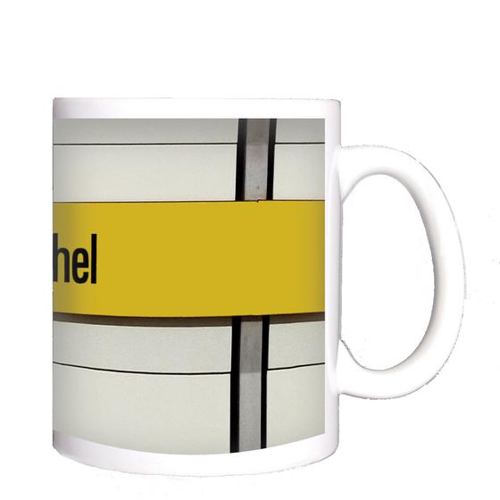 U-Bahnhof Lehel Kaffeetasse - schwarze Schrift auf gelbem Streifen, vor weißer Plattenwand