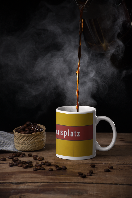 U-Bahnhof Kolumbusplatz Kaffeetasse - weiße Schrift auf dunkelrotem Streifen, vor gelber Plattenwand