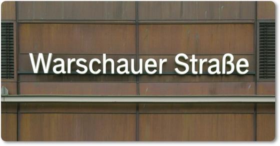 Kühlschrankmagnet mit Aufdruck der originalgetreuen Gestaltung des Berliner Umsteigebahnhofs S-U-Bahn Warschauer Strasse - weisse Buchstaben auf einer Wand aus rostig-braunen Metallplatten