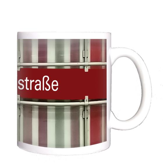 U-Bahnhof Dülferstraße Kaffeetasse - weiße Schrift auf rotem Schild auf Metallgestell, vor Streifenhintergrund in diversen Rottönen