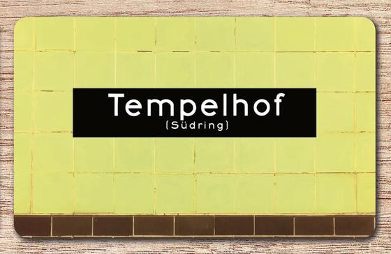 U-Bahnhof Tempelhof Frühstücksbrettchen - weiße Schrift auf schwarzem Schild, vor gelber Fliesenwand