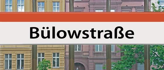 U-Bahnhof Kaffeetasse Bülowstrasse - schwarze Schrift auf weißem Schild mit orangem Streifen, an Bahnhofsfenster befestigt mit rotem und gelbem Haus im Hintergrund